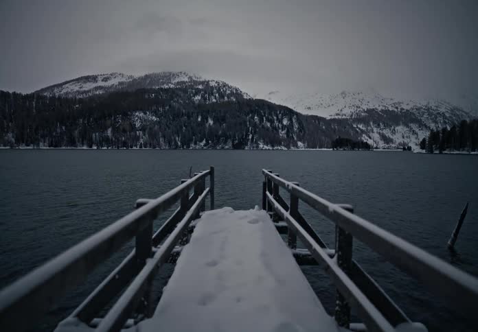 Snowy metal pier over a lake with mountains in the background on a cloudy day