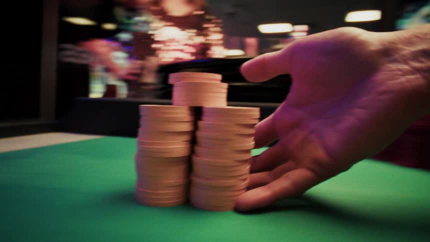 Hand carefully arranges stacked poker chips on a green table and takes it to another hand