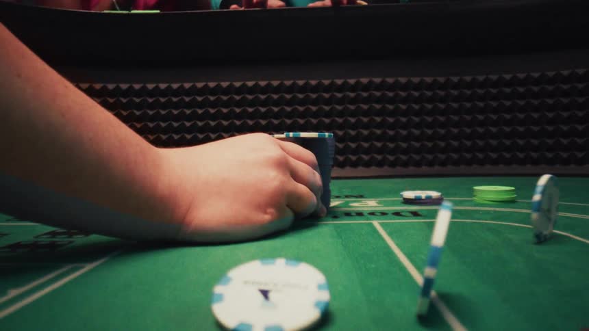 Hand dragging poker chips across a table and in the background peoples arms cheering