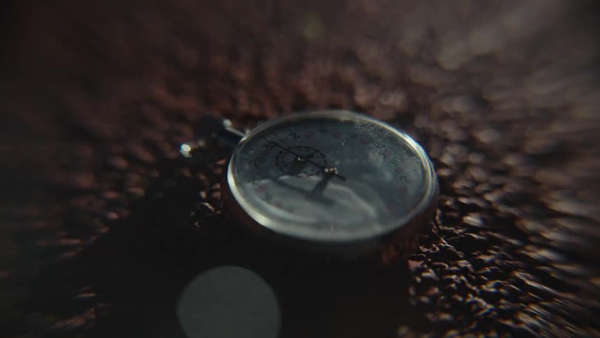 A vintage stopwatch resting on a textured dark surface with a soft out of focus background