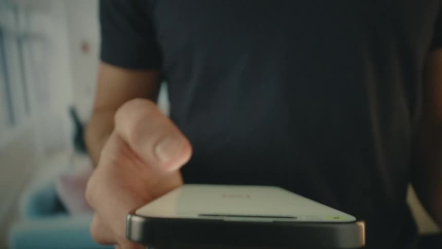 A man standing in a room is scrolling on his phone with his thumb