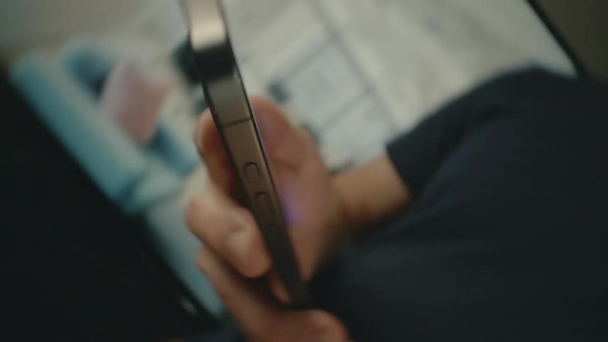 A person is holding a smartphone initially out of focus and brings it into focus in their hand showing the side and the screen
