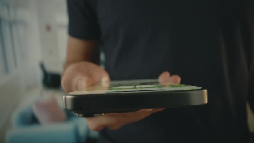 A persons hands are shown holding a smartphone with a social media feed displayed on its screen with a blurred background while using it