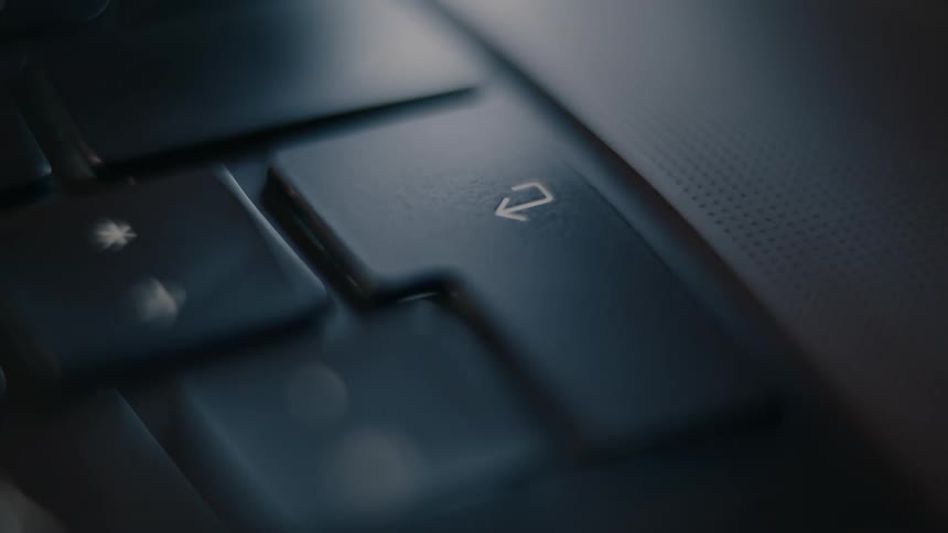 A finger pressing the enter key on a dark laptop keyboard