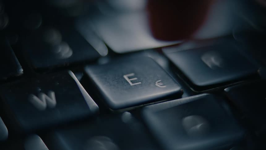 A close up slightly blurry view of a keyboard focuses on the e key which is repeatedly pressed by a finger