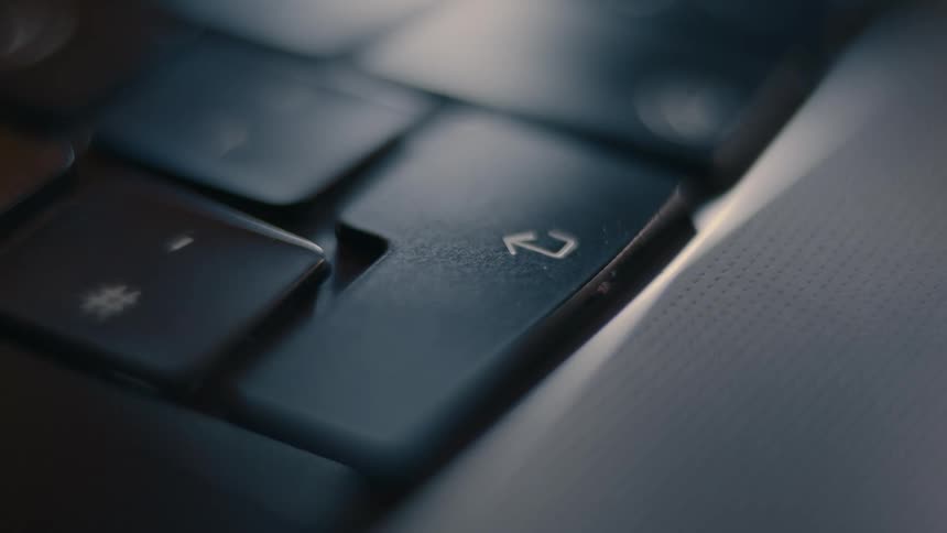 A finger taps the enter key on a laptop keyboard in a close up slightly out of focus shot