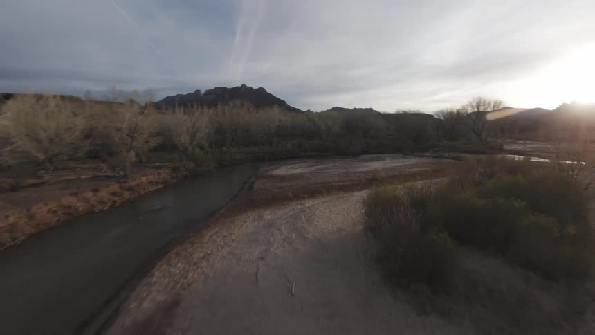 Winding river surrounded by sparse vegetation and the sun on the horizon
