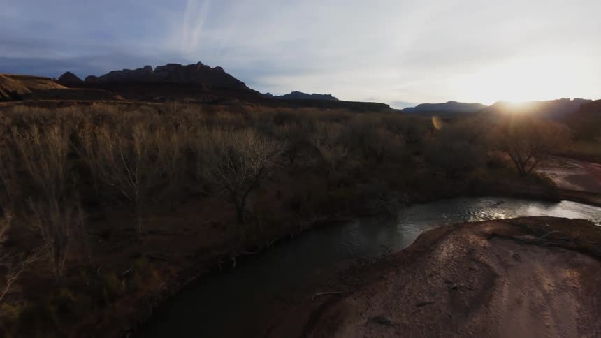 Aerial shot of a winding river surrounded by vegetation and the sun rising on the horizon