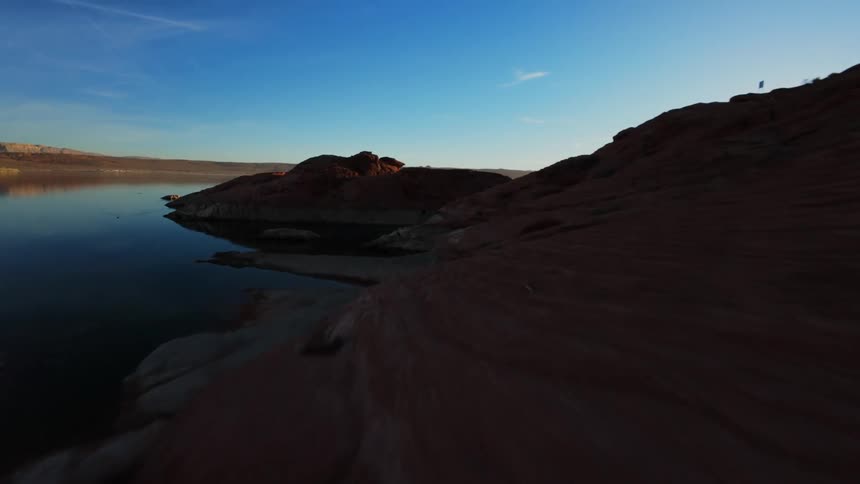 A sunset over a still lake with rugged red cliffs framing the scene and a small island silhouetted in the distance