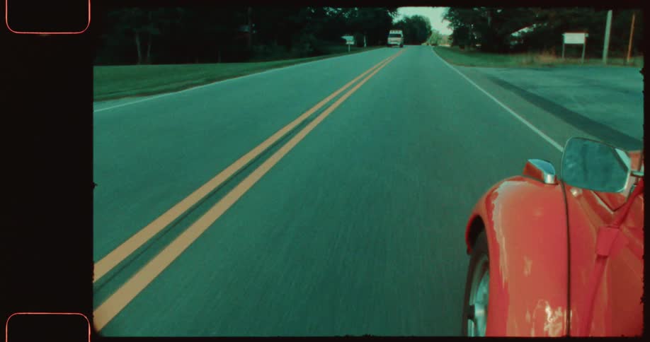 The exterior of a red car driving on an asphalt street with a yellow stripe in the middle and cars passing in the opposite direction