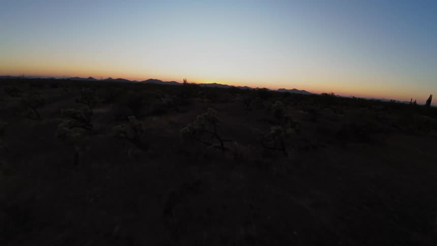 Desert landscape at dusk with low horizon outlining dark mountains and gradient sky ranging from orange to deep blue