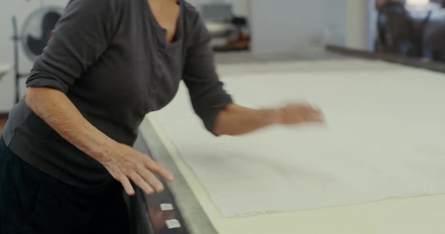 Blonde woman smoothing material on a work surface stops to give directions