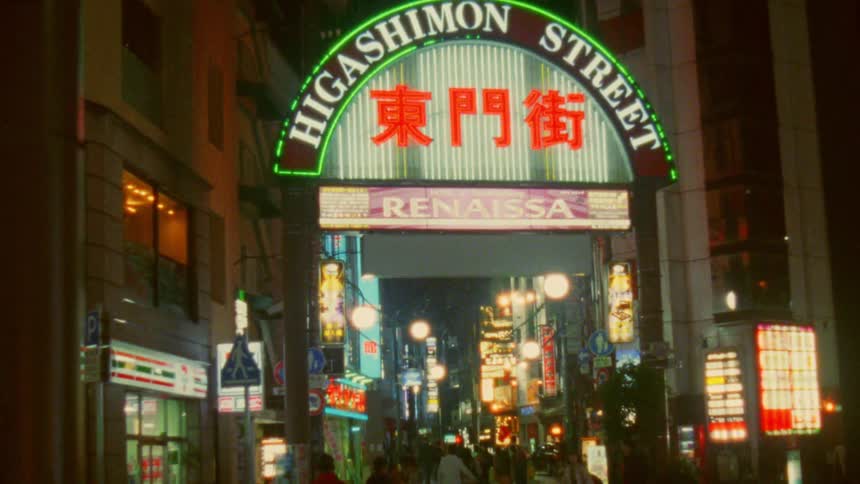 Illuminated billboard with asian letters in a city and pedestrians walking