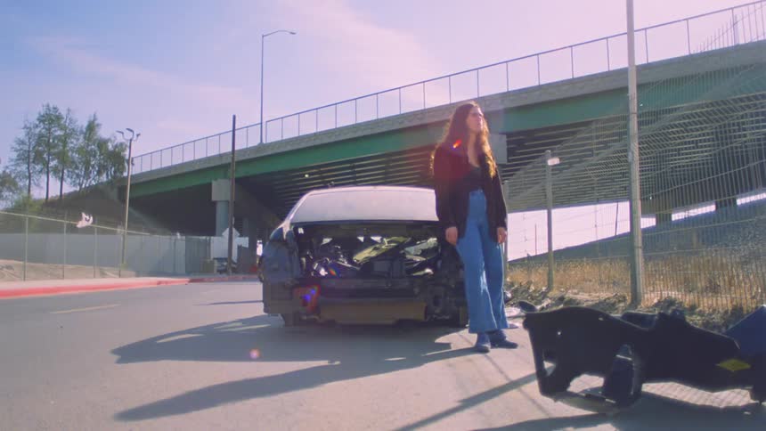 A woman is standing and leaning against a car that has been stripped