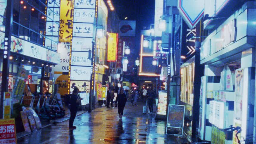 A vibrant illuminated street in an urban area at night with neon signs in japanese wet pavement reflecting the lights and people walking along the sidewalk