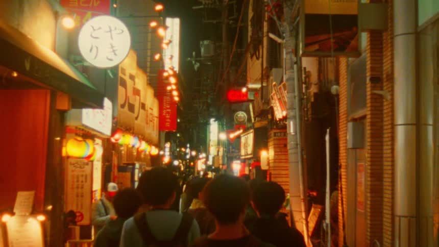 Crowd of pedestrians walk down a lit alley with shops and restaurants at night