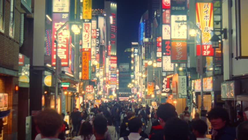 A bustling brightly lit street in a city at night filled with a crowd of people and lined with numerous colorful signs and advertisements in japanese