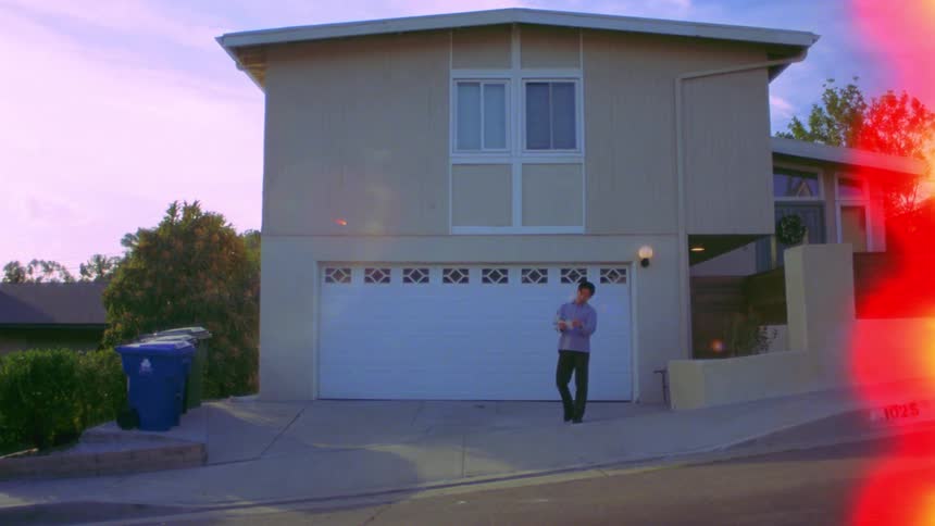 A person collecting and reading mail on a sloped street in front of a house