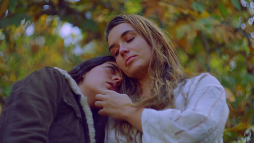 A young couple standing close together outdoors with one person resting their head on the others shoulder