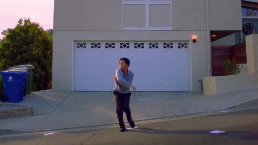 A man is doing an interpretive dance in the street in front of a house