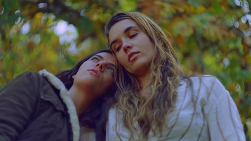 A young couple standing close together outdoors with one person resting their head on the others shoulder