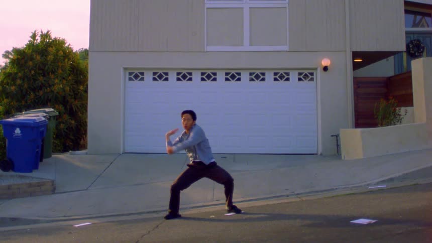 A man does an interpretive dance in the street in front of a house