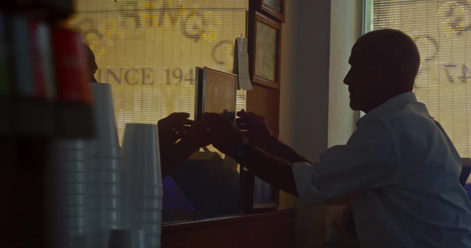 Man in a restaurant reaches up for a photograph attached to a mirror