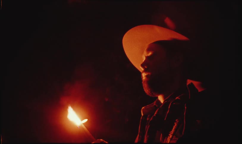 A man with a hat on is holding a stick that is on fire
