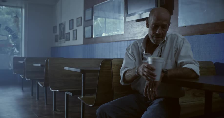 An older man is sitting in a booth at a restaurant and drinking from a cup