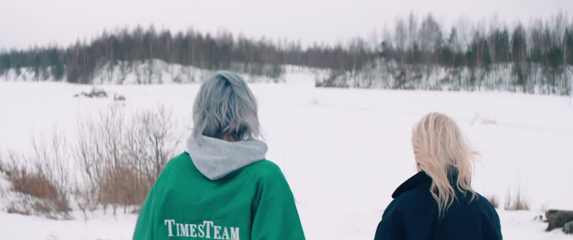 Two women with lightcolored hair are walking outdoors in a snowy landscape
