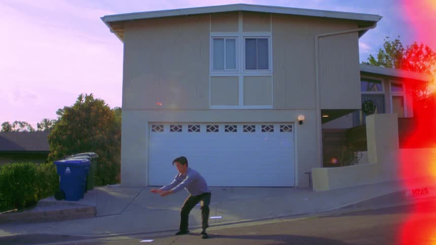 A person throws papers in the air and starts dancing on a sloped street in front of a house