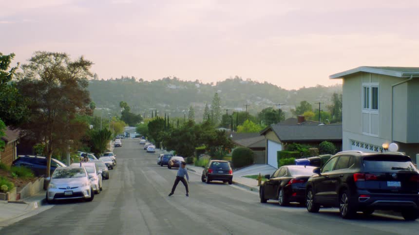 A man dances on a neighborhood street tossing sheets of paper into the air as evening falls