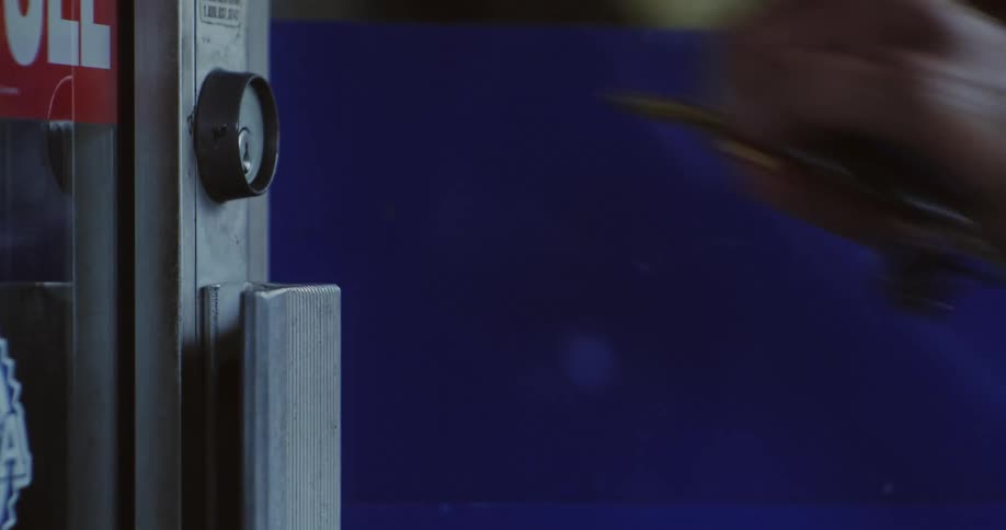 An elderly person puts the key into the lock of a business door and unlocks it
