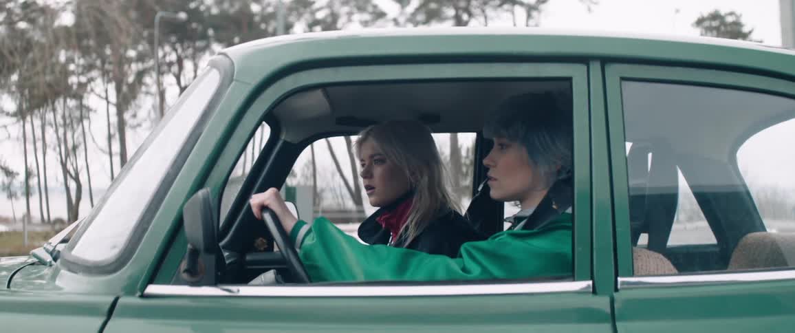 Two young women inside a moving green classic vehicle