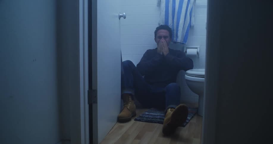 A sad or depressed person is sitting on the bathroom floor with a prescription pill bottle on the toilet seat