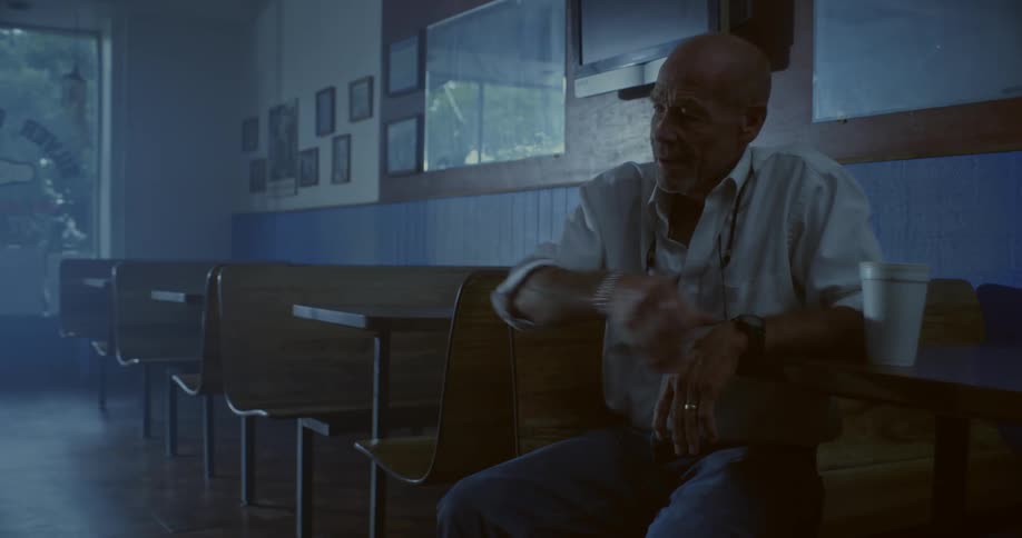 Man sitting at a table in a cafeteria thinking drinking from a disposable cup