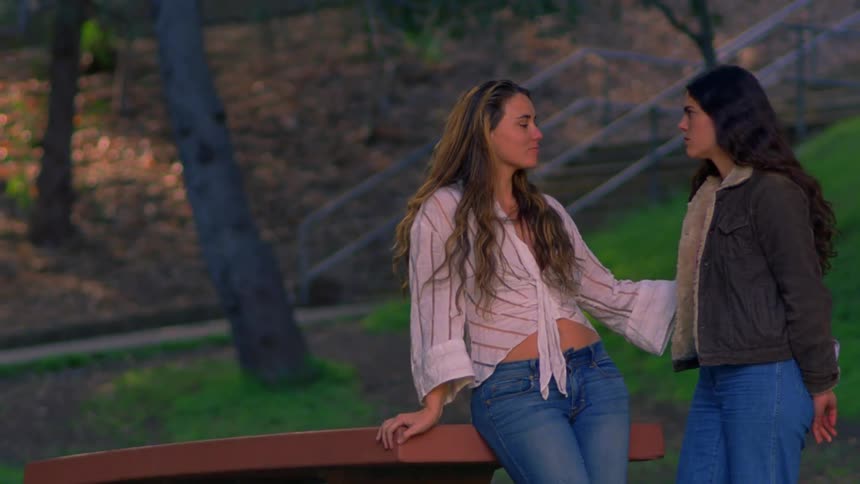 A couple standing close together at a park leaning against a picnic table