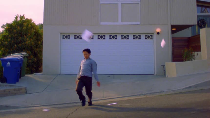 A person throws papers in the air and starts dancing on a sloped street in front of a house