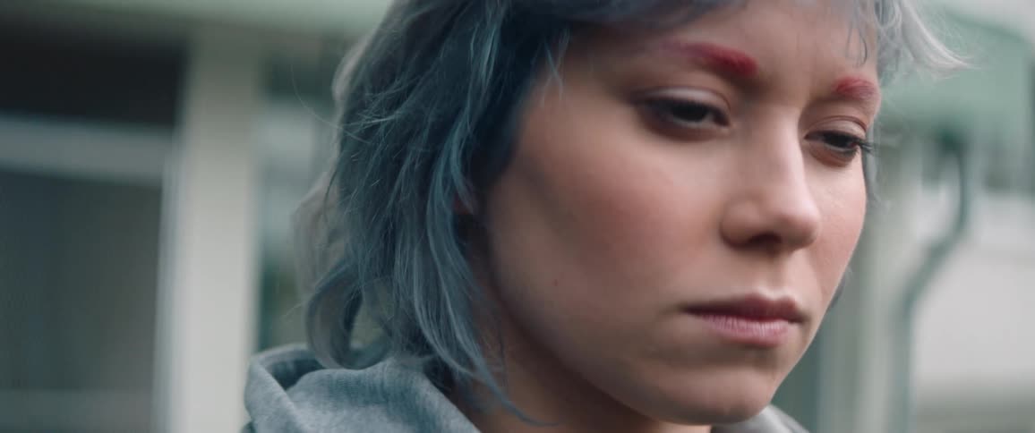 A woman with dyed blue hair and red eyebrows slowly opening her eyes