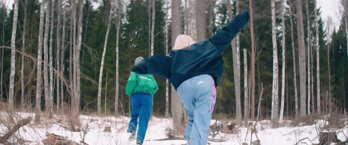 Two women with lightcolored hair are running towards a forest in a snowy landscape