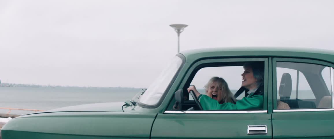 Two women laugh as they drive down a road