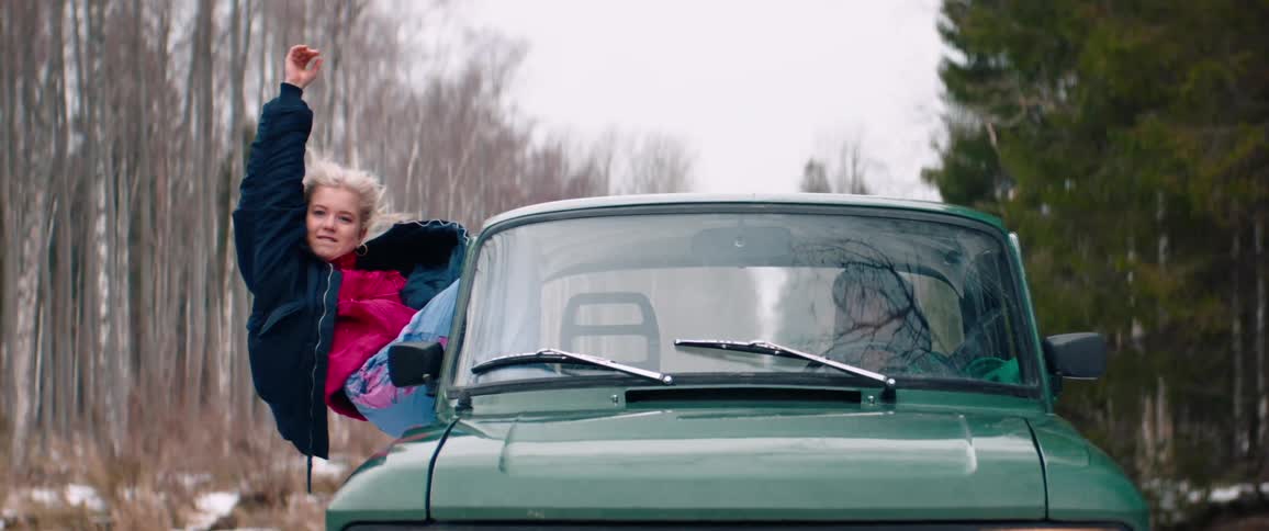 Blonde woman enjoys partially exiting through the window of a moving green car