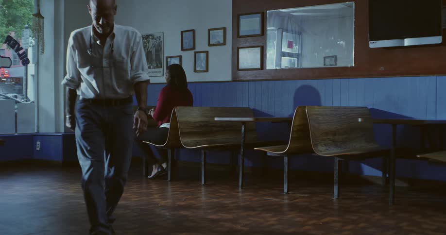 A man in a white shirt and jeans walks away from a woman sitting at a table in a diner