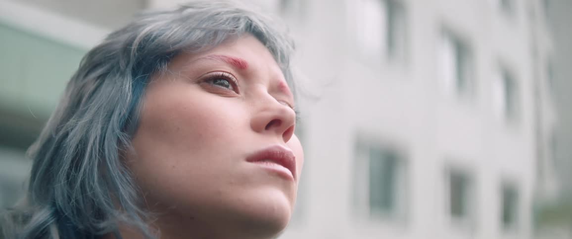 A young woman with gray hair stands outdoors in front of a building with windows