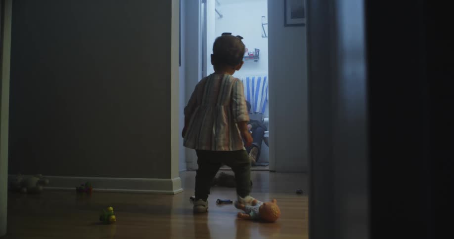 A man sits on the floor in the bathroom as a child walks by