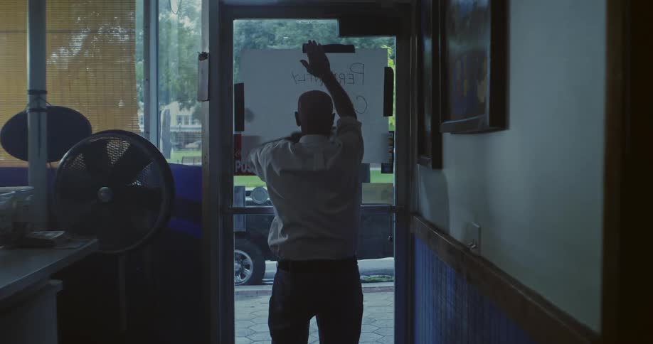 A man hangs a hand written sign on the shop door