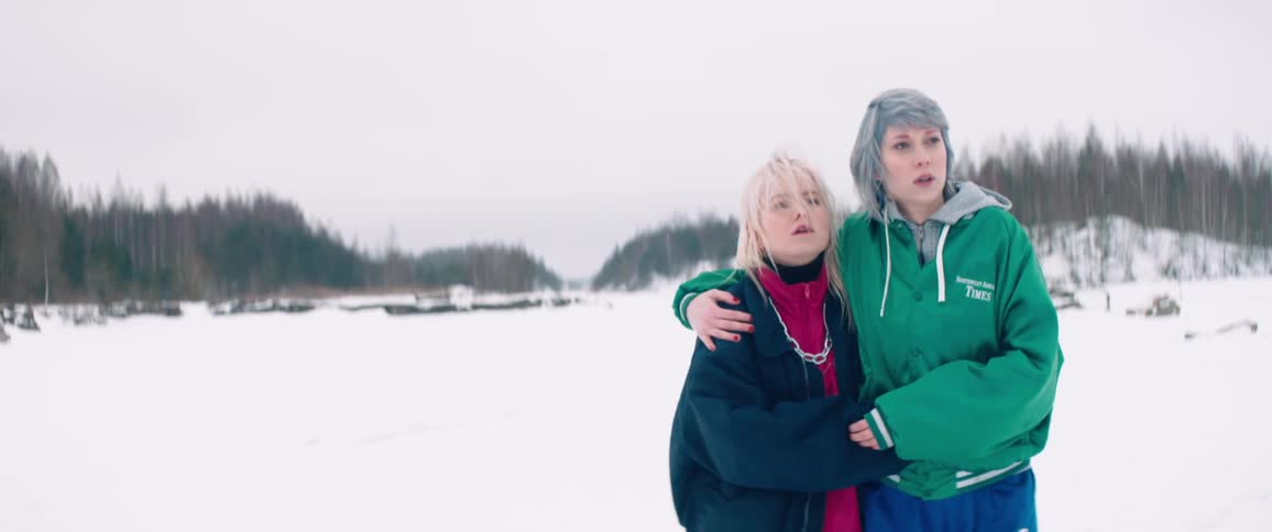 Two women share an embrace as they walk through a snowy field