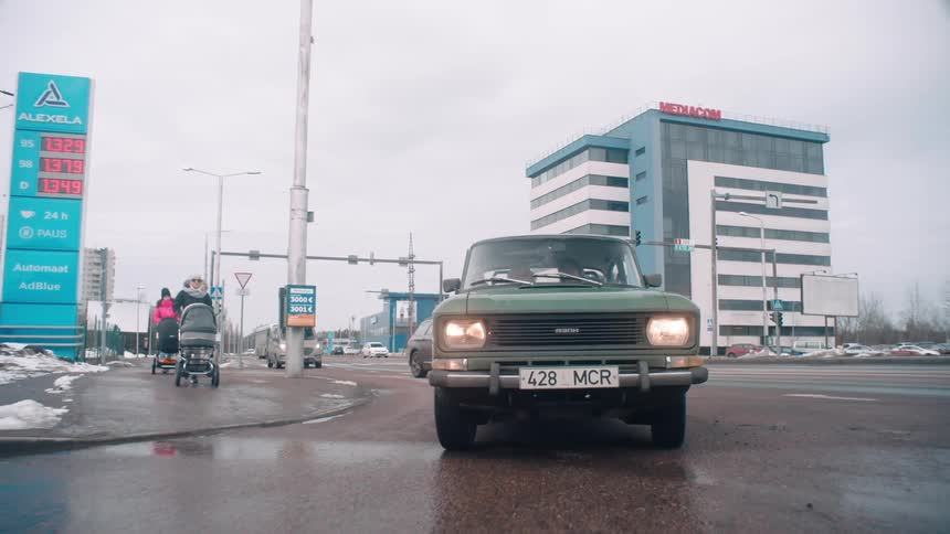 Green classic car driving through the streets of a city in winter