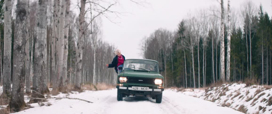 A woman sits in the open window of a car as it drives down a snowy road