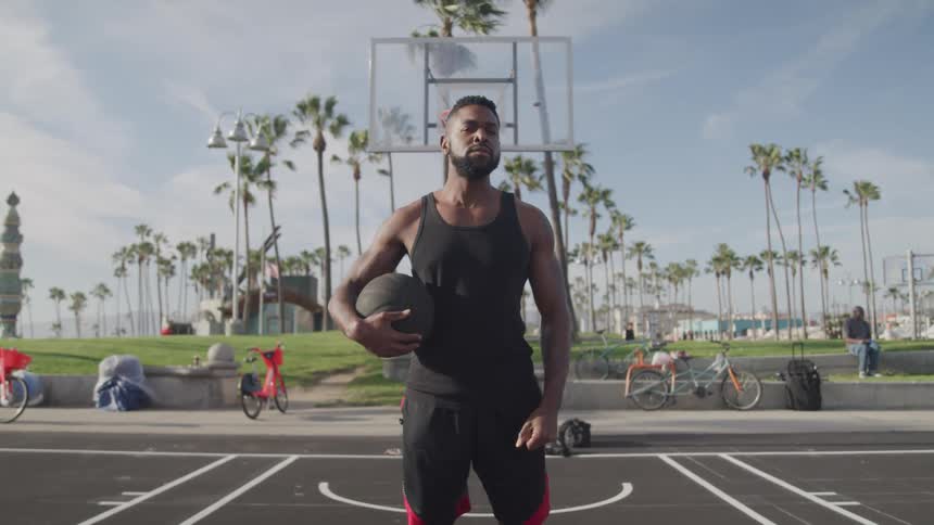 Man standing looking around while holding a basketball on an outdoor court